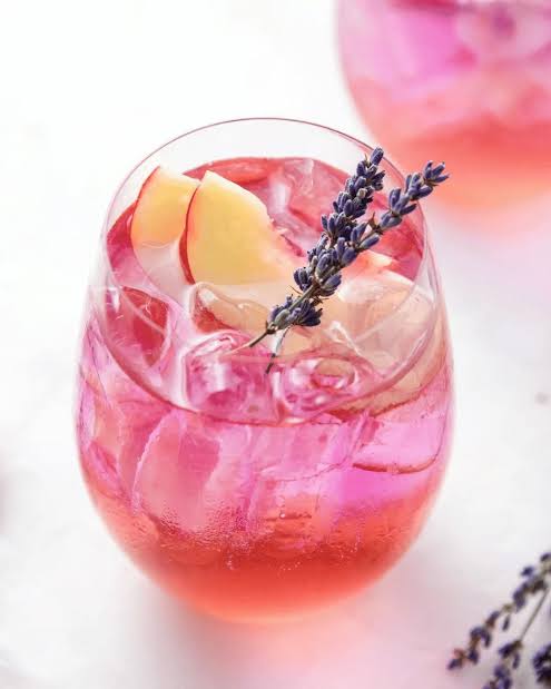 Iced pink sunset drink with peach slices, lavender sprig and ice